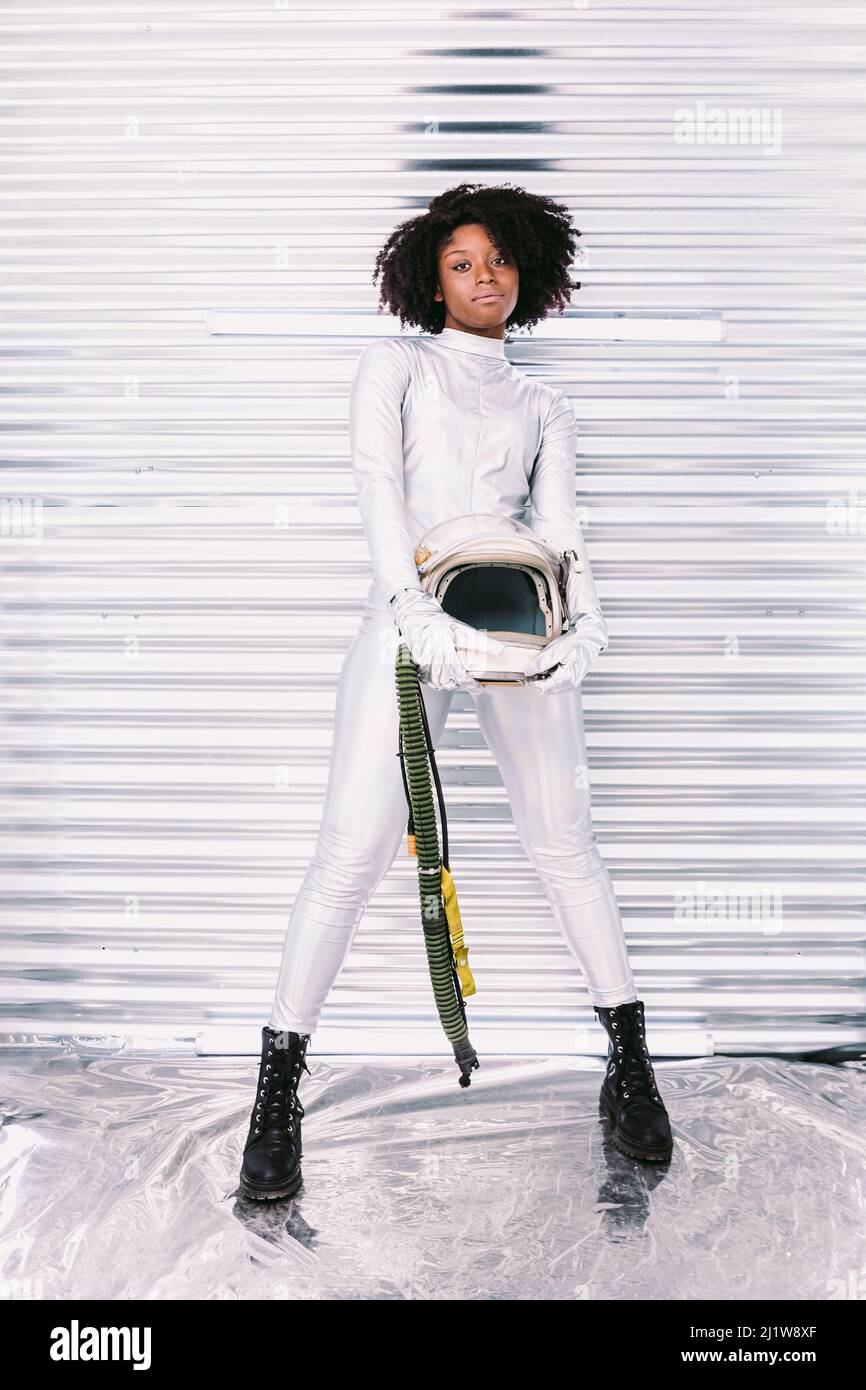Charmante femme afro-américaine avec casque en costume d'astronaute blanc regardant la caméra tout en se tenant dans un vaisseau spatial blanc sur fond clair Banque D'Images