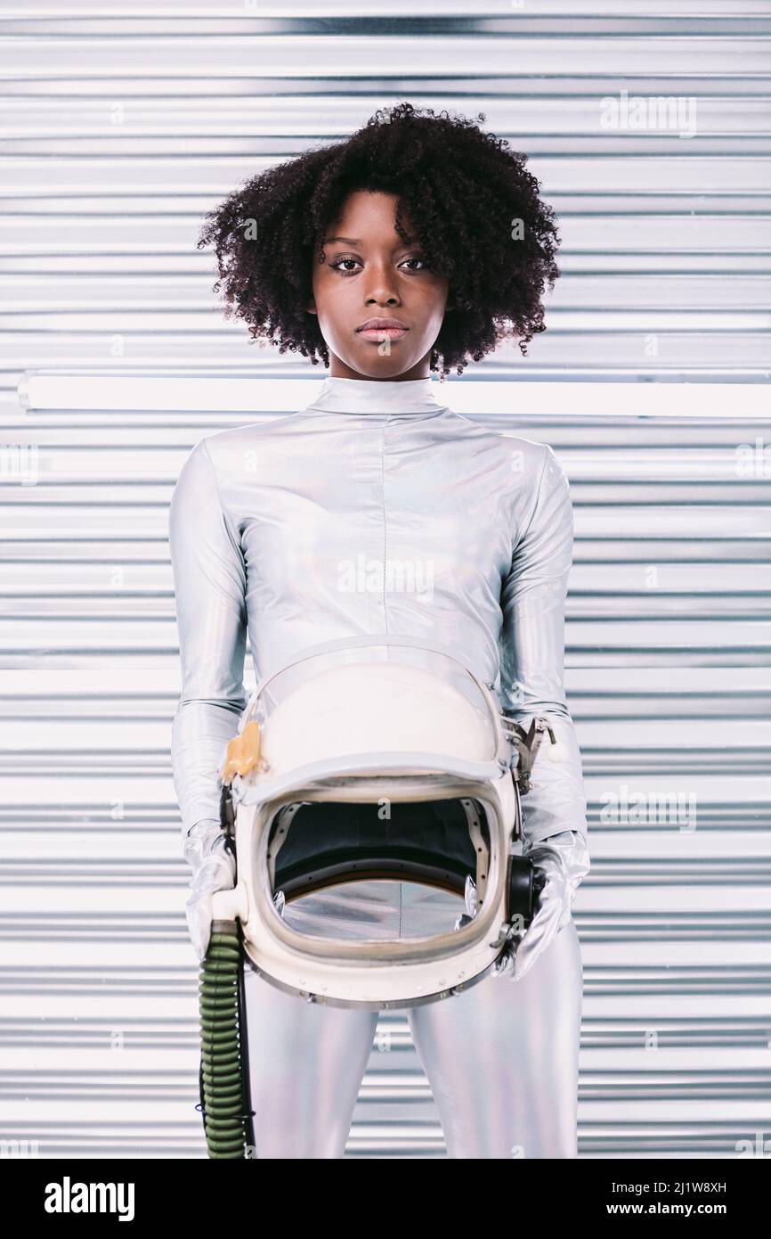 Charmante femme afro-américaine avec casque en costume d'astronaute blanc regardant la caméra tout en se tenant dans un vaisseau spatial blanc sur fond clair Banque D'Images