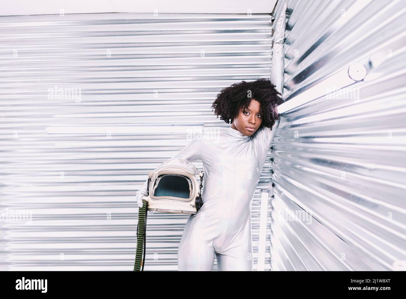 Charmante femme afro-américaine avec casque en costume d'astronaute blanc regardant la caméra tout en se tenant dans un vaisseau spatial blanc sur fond clair Banque D'Images