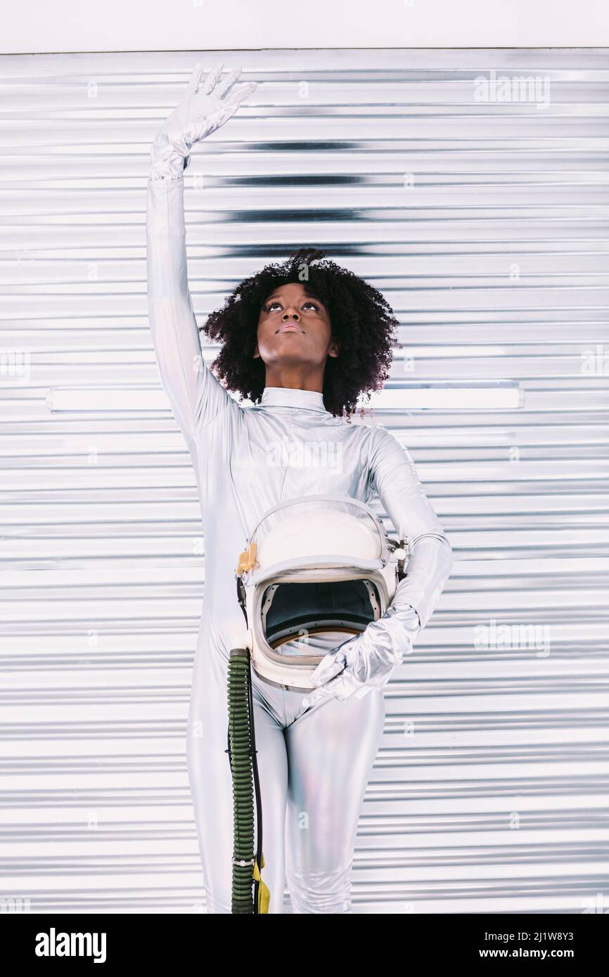 Charmante femme afro-américaine avec casque en costume d'astronaute blanc, regardant dans un vaisseau spatial blanc sur fond clair Banque D'Images