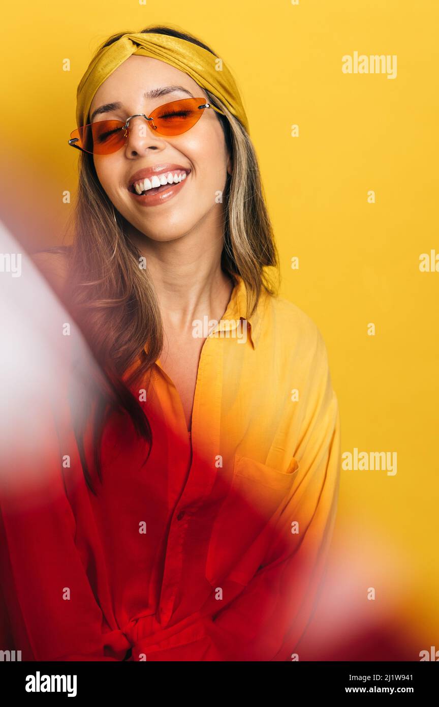 Vue à travers le verre rouge sur une femme tendance dans une tenue  lumineuse et des lunettes de soleil souriant gaiement sur fond jaune dans  le studio Photo Stock - Alamy