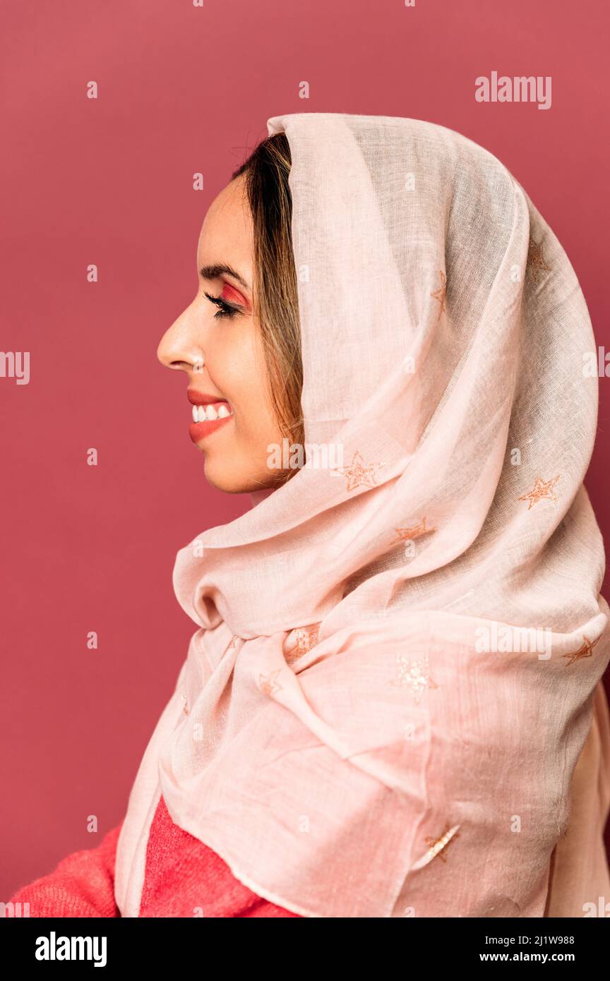 Vue latérale d'une femme optimiste avec maquillage coloré et foulard léger  sur fond rose en studio Photo Stock - Alamy