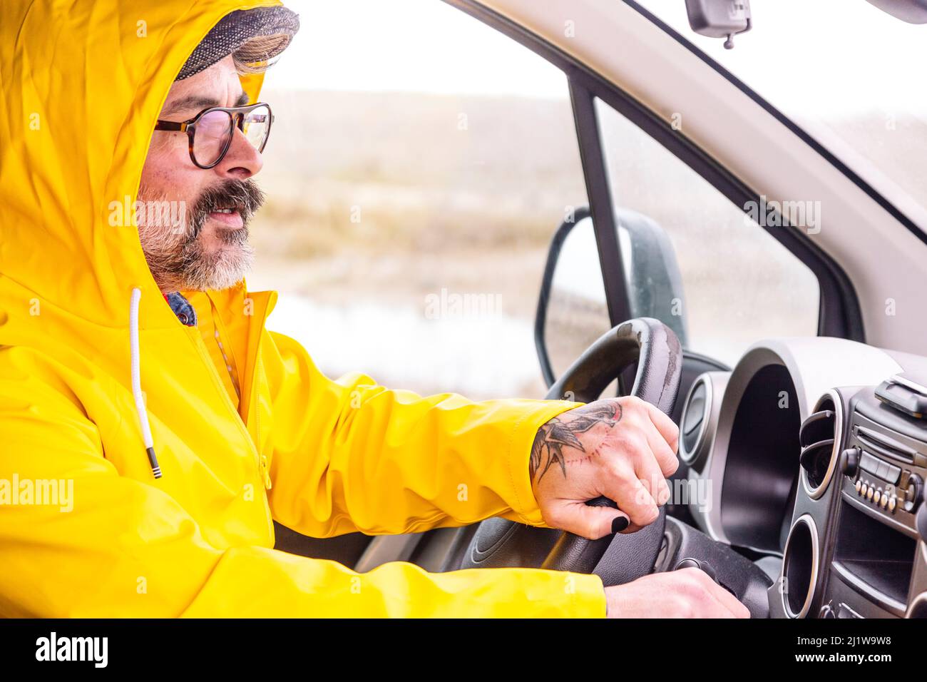 Conducteur mâle barbu avec les mains sur le volant conduisant la voiture en campagne Banque D'Images