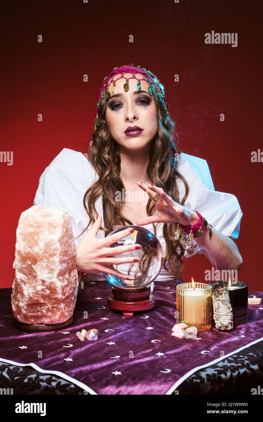 Charmante femme au regard de la fortune, avec un maquillage qui devine l'avenir à la table, avec un ballon magique et des bougies allumées près du cristal Banque D'Images