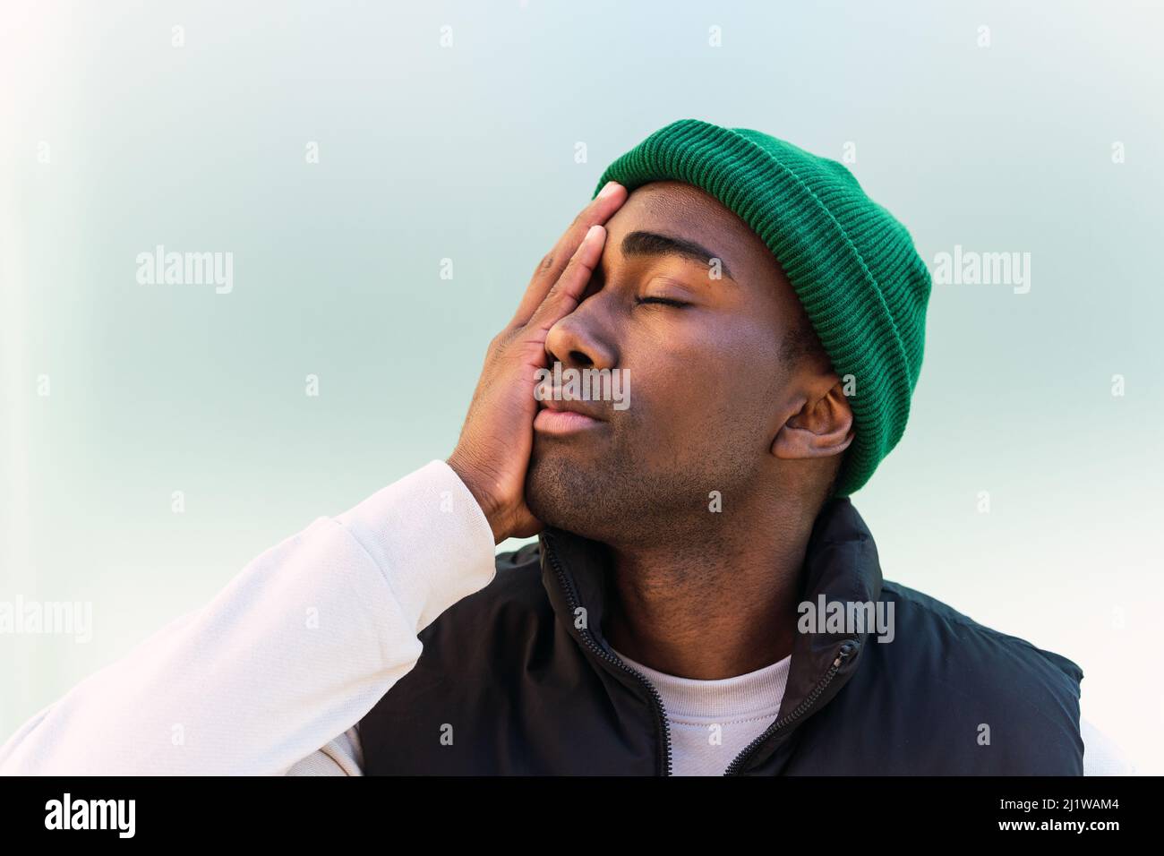 Contenu Afro-américain homme dans la casquette verte touchant le visage sur  fond vert et les yeux de fermeture Photo Stock - Alamy