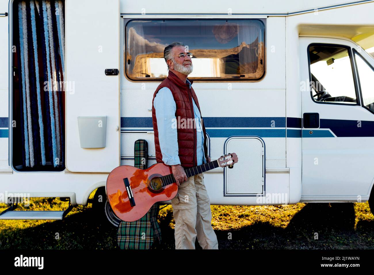 Vue latérale de l'homme senior avec guitare roulant le long de la voiture RC garée dans la campagne pendant le voyage Banque D'Images