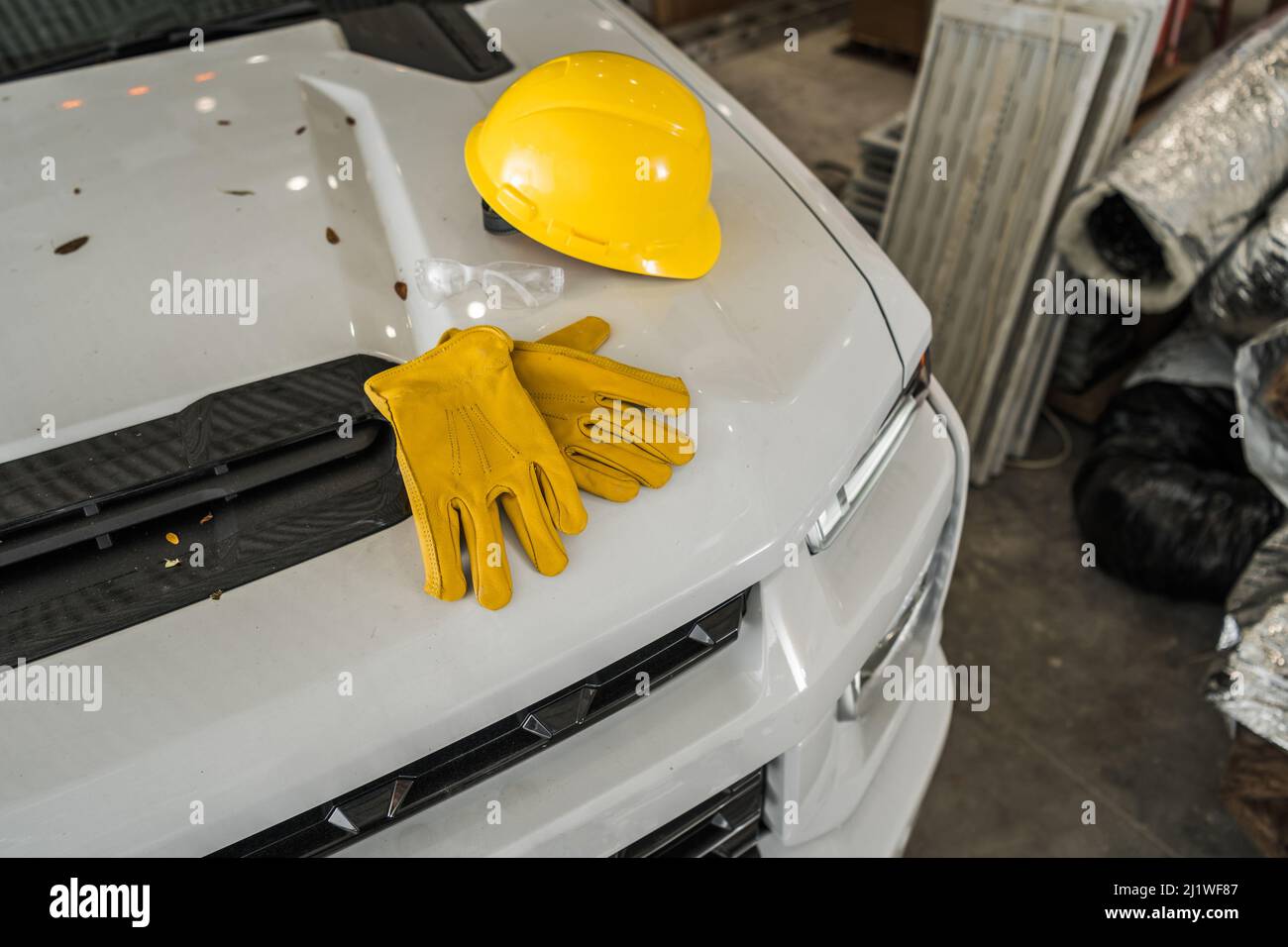 Sécurité de la construction chapeau rigide en plastique jaune et gants de travail sur capot de ramassage blanc gros plan. Thème industriel. Banque D'Images