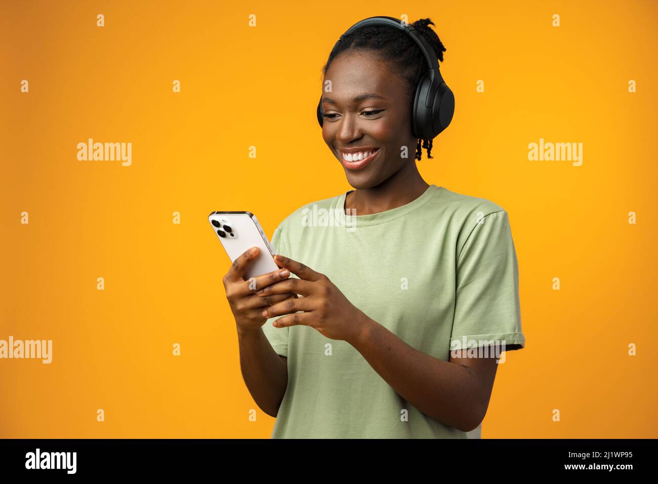 Bonne jeune Afro-américaine femme écoutant de la musique dans des écouteurs sur fond jaune Banque D'Images