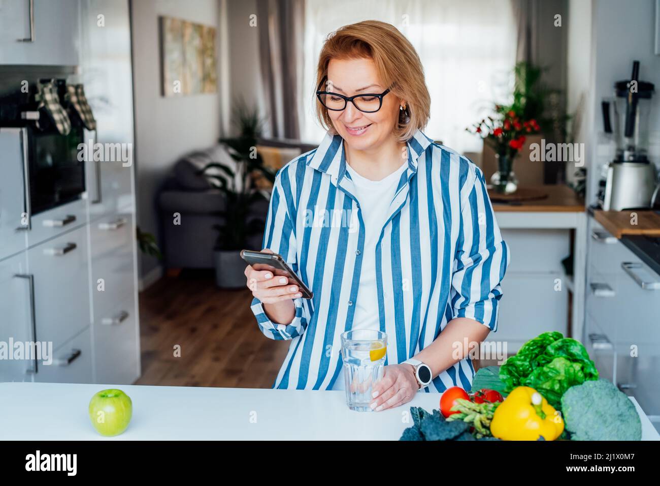 Régime alimentaire sain. Femme prenant des notes, tapez son menu dans l'application téléphone, assis au-dessus de la table avec des légumes frais dans sa cuisine. Végétarien, p Banque D'Images