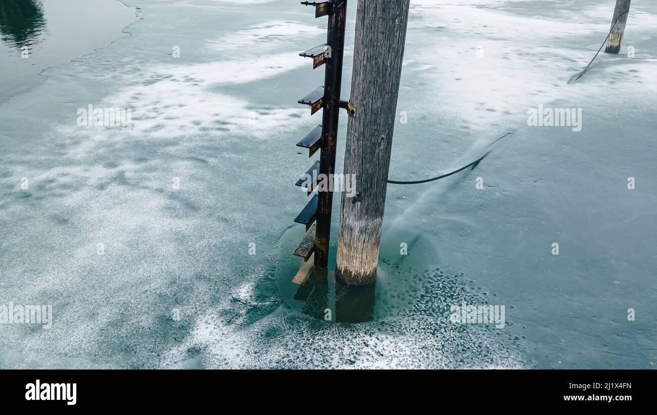 Un étang glacé avec une vieille échelle sur un poteau s'étendant dans l'eau Banque D'Images