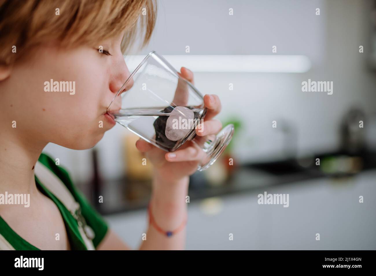 Une jeune fille boit de l'eau à partir d'un verre avec des pierres de shungite. Banque D'Images