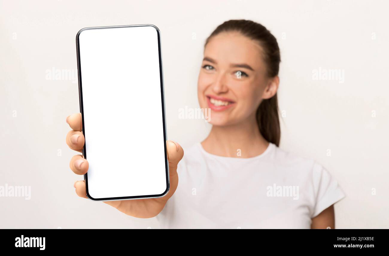 Bonne femme caucasienne tenant un smartphone avec écran blanc vierge et le montrant à l'appareil photo, maquette Banque D'Images