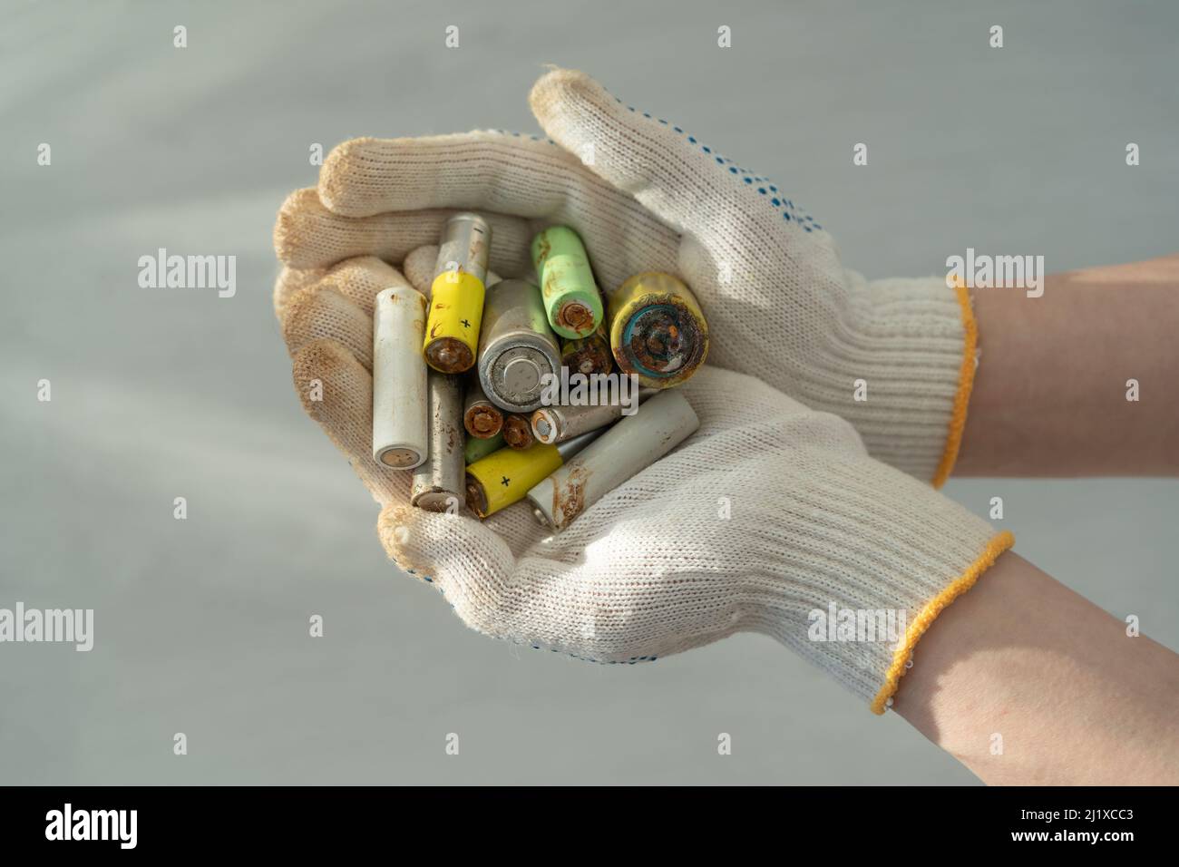 Gros plan des mains des femmes dans des gants de protection en coton tenant le tas de piles alcalines usagées Banque D'Images