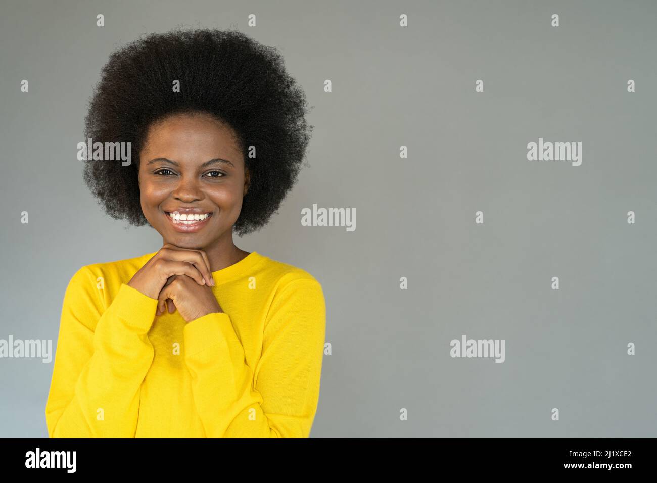 Souriant Afro-américaine fille porter un chandail jaune posant sur le mur gris dans le studio, regardant la caméra Banque D'Images