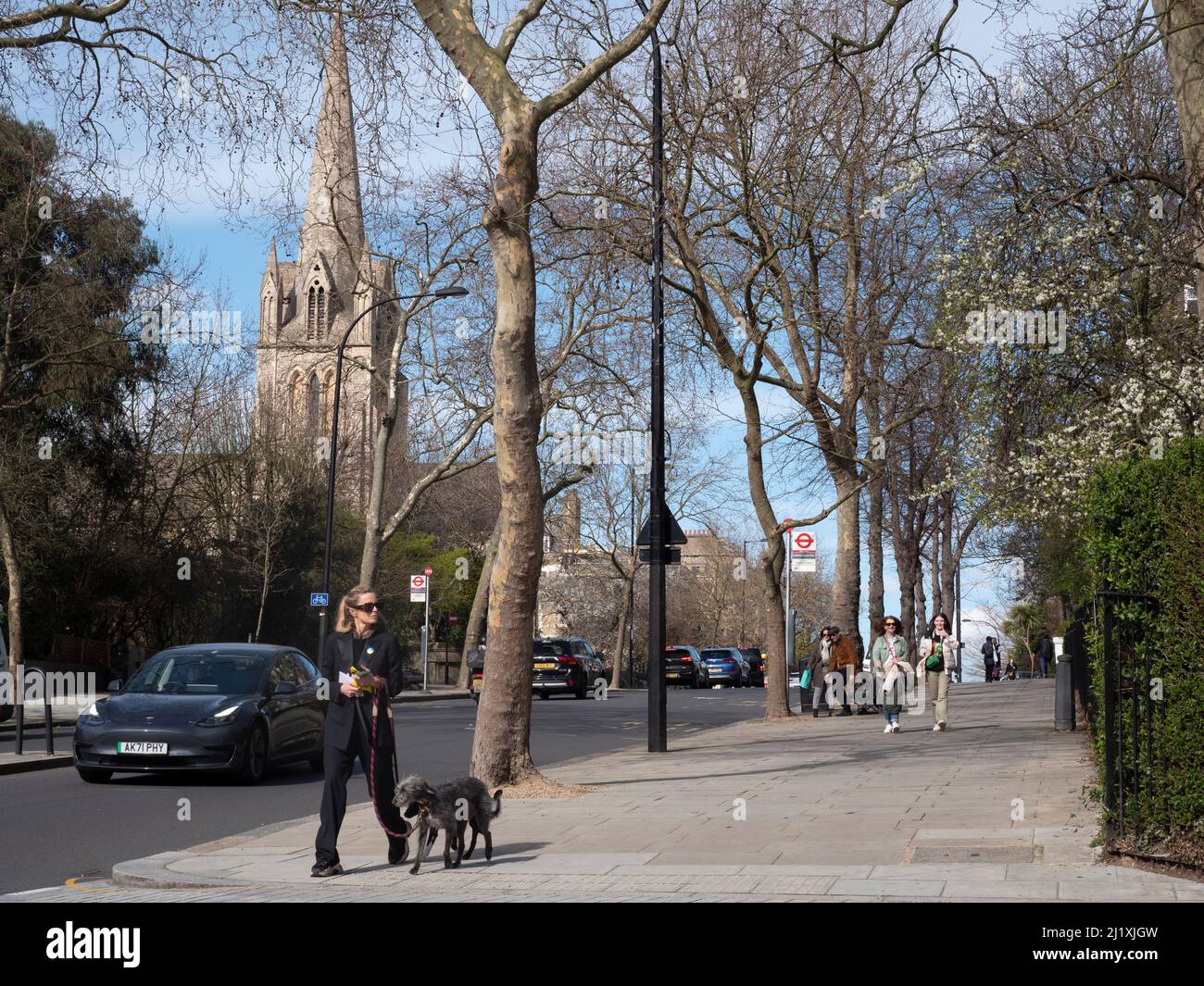 Des piétons et des marcheurs pour chiens marchent sur le trottoir de Ladbroke Grove avec l'église St Johns en arrière-plan dans le quartier royal de Kensington et Chelsea Banque D'Images