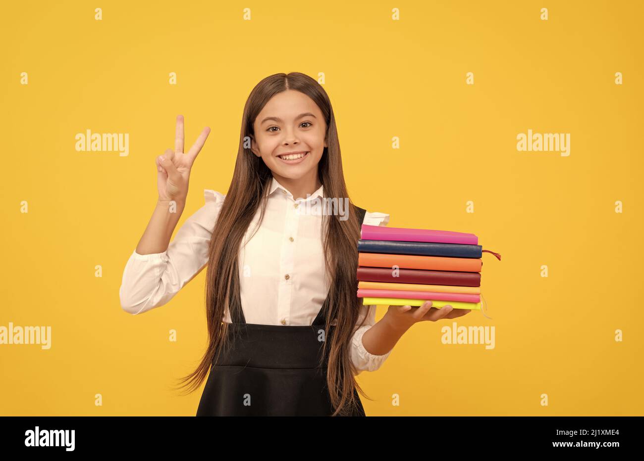 bonne adolescente fille dans l'uniforme d'école tenir pile de livre montrer la paix geste, éducation Banque D'Images