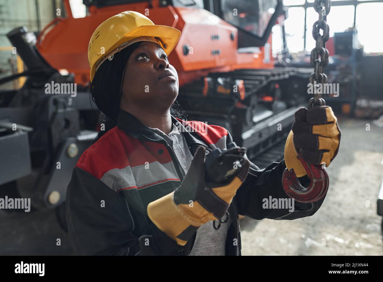 Femme africaine en uniforme et casque de travail utilisant le panneau de commande pour travailler avec une grue dans un entrepôt Banque D'Images