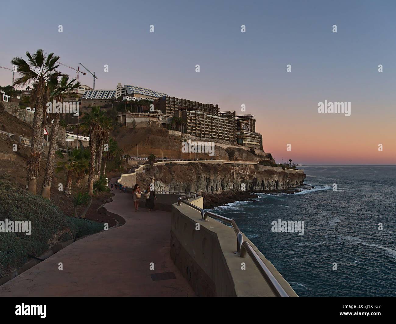 Les gens appréciant la soirée après le coucher du soleil sur la promenade dans la station de vacances Puerto Rico, le sud de Gran Canaria, les îles Canaries, Espagne avec grand hôtel. Banque D'Images