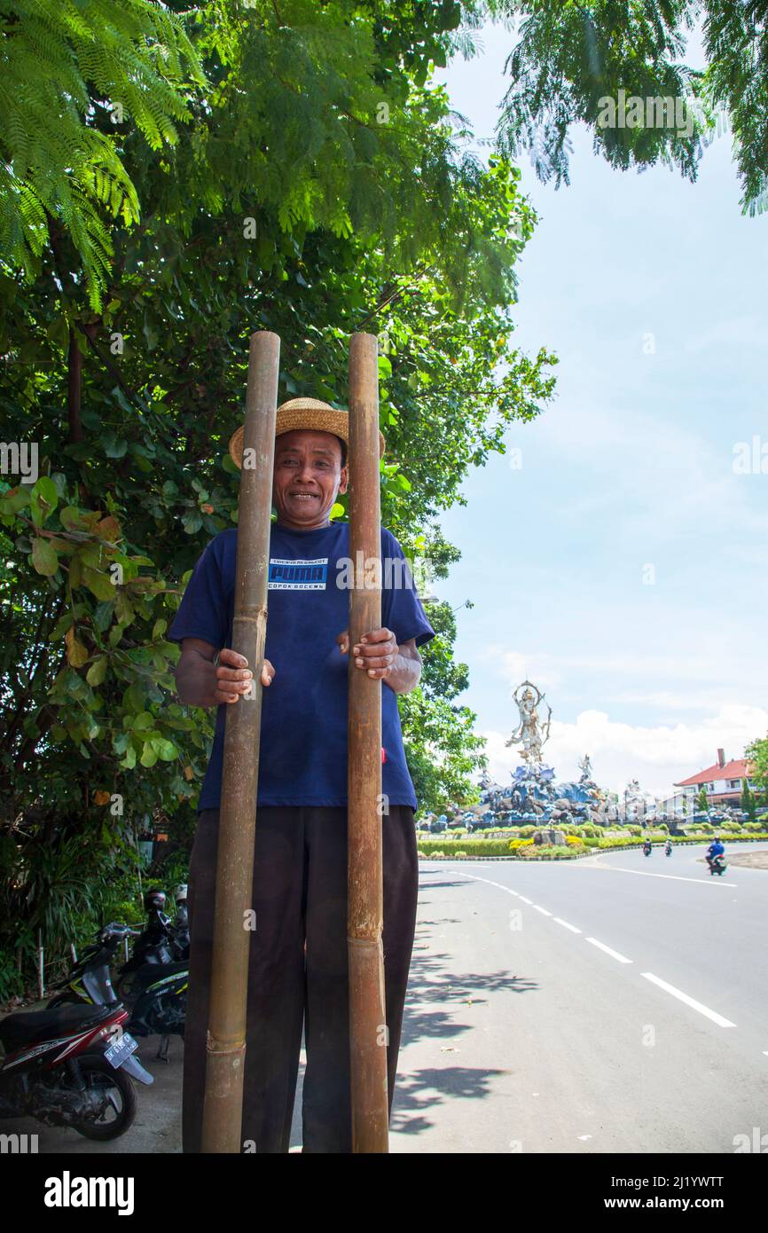 Un homme âgé qui se produit en marchant sur des pilotis sur le bord de la route près de Denpasar Bali, en Indonésie. Banque D'Images