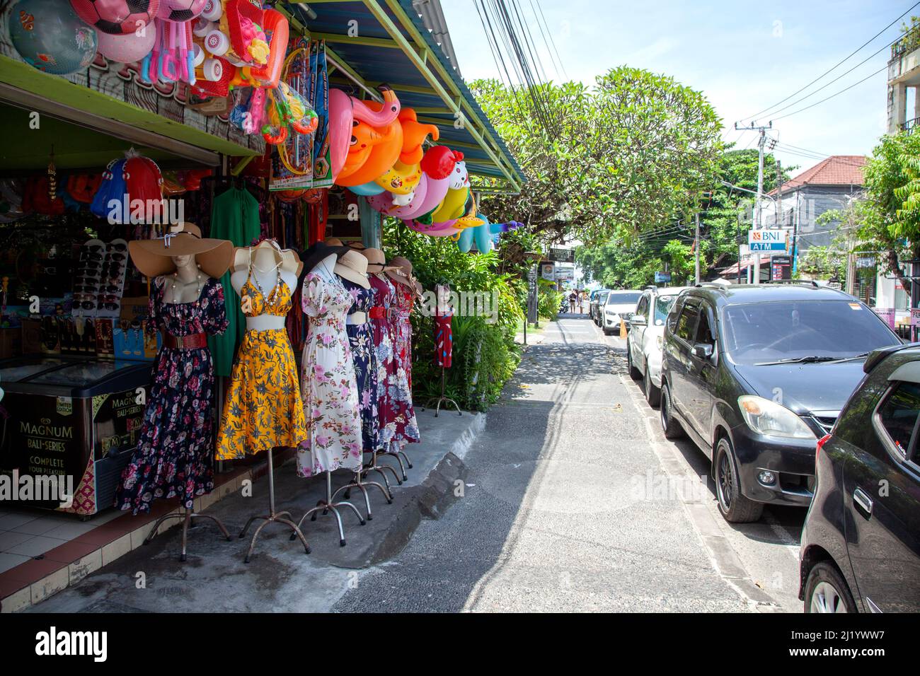 Une boutique vendant des vêtements et des jouets de plage sur Jl. Accrochez Tuah au nord de Sanur, Bali avec des voitures garées le long du bord du trottoir. Banque D'Images