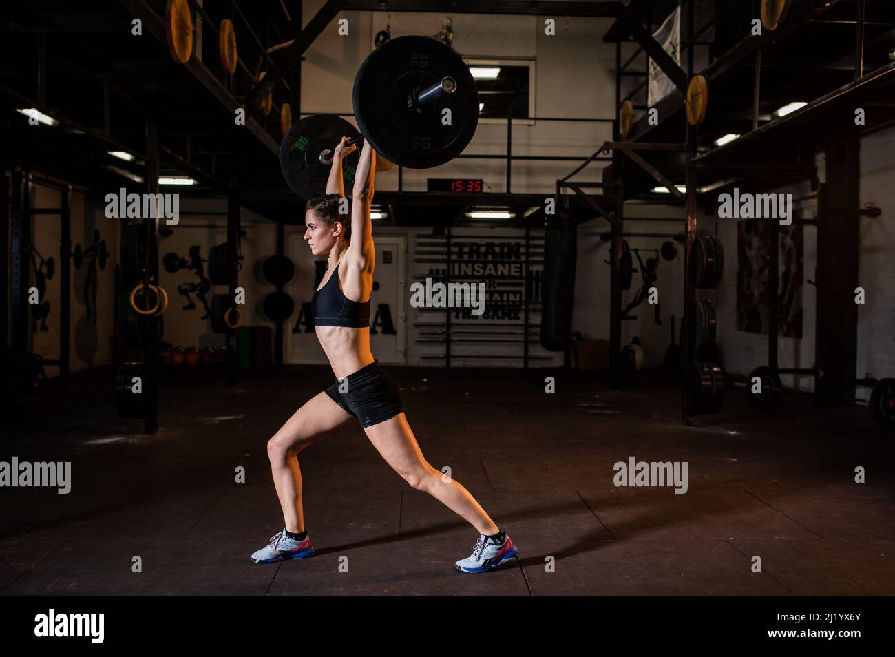 Une femme musclée attrayante soulève des poids dans une salle de sport moderne et entièrement équipée. Elle prend soin de sa santé et de son apparence. Formation individuelle. Banque D'Images