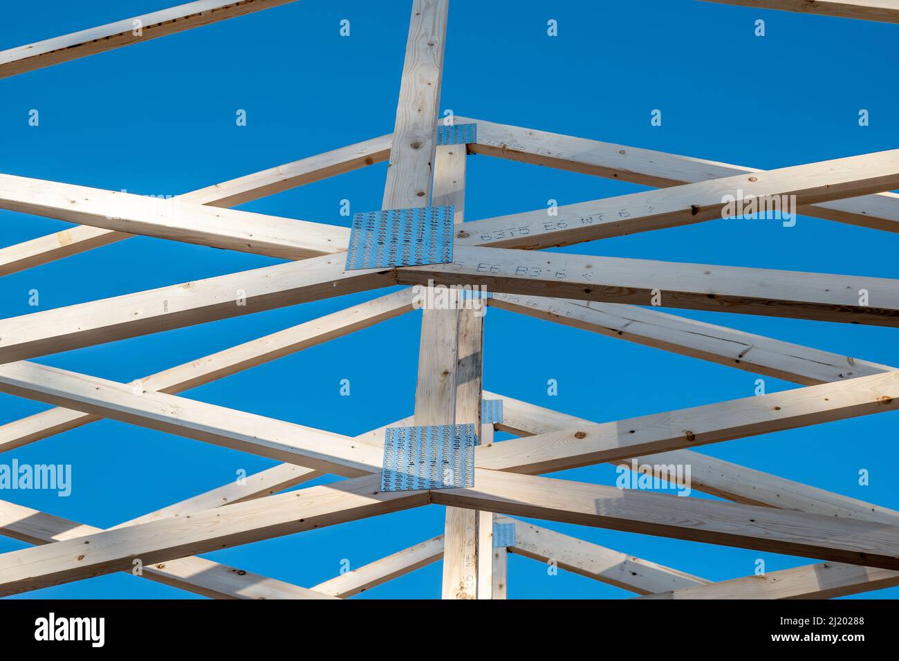 Fermes de toit en bois et plaques de connexion en métal, partiellement ombragées, sur un nouveau projet de construction de maison avec ciel bleu en arrière-plan. Banque D'Images