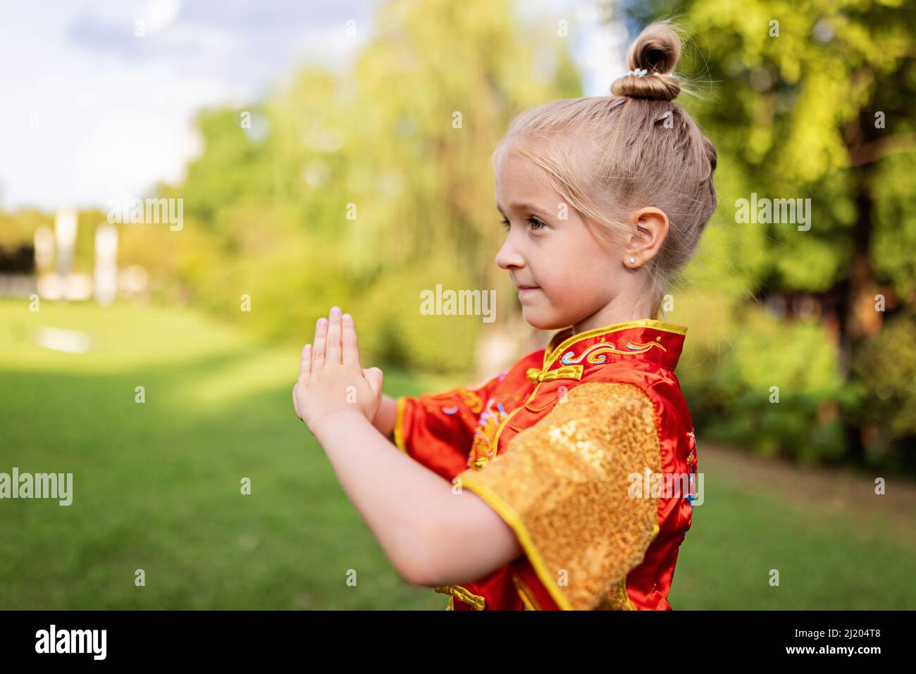 Mignonne petite fille caucasienne de sept ans dans le rouge sport wushu uniforme s'exerçant dans le parc le jour d'été. Portrait du style de vie d'un enfant combattant kung fu Banque D'Images