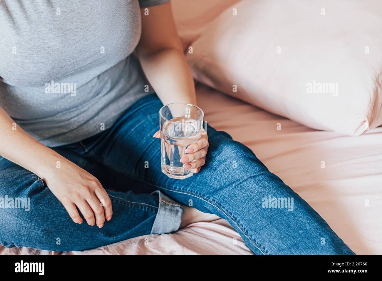 Une femme s'assoit dans son lit et tient un verre d'eau propre dans ses mains. Journée mondiale de l'eau. Concept de soins de santé. Boire de l'eau le matin pour stimuler le métabolisme. Banque D'Images