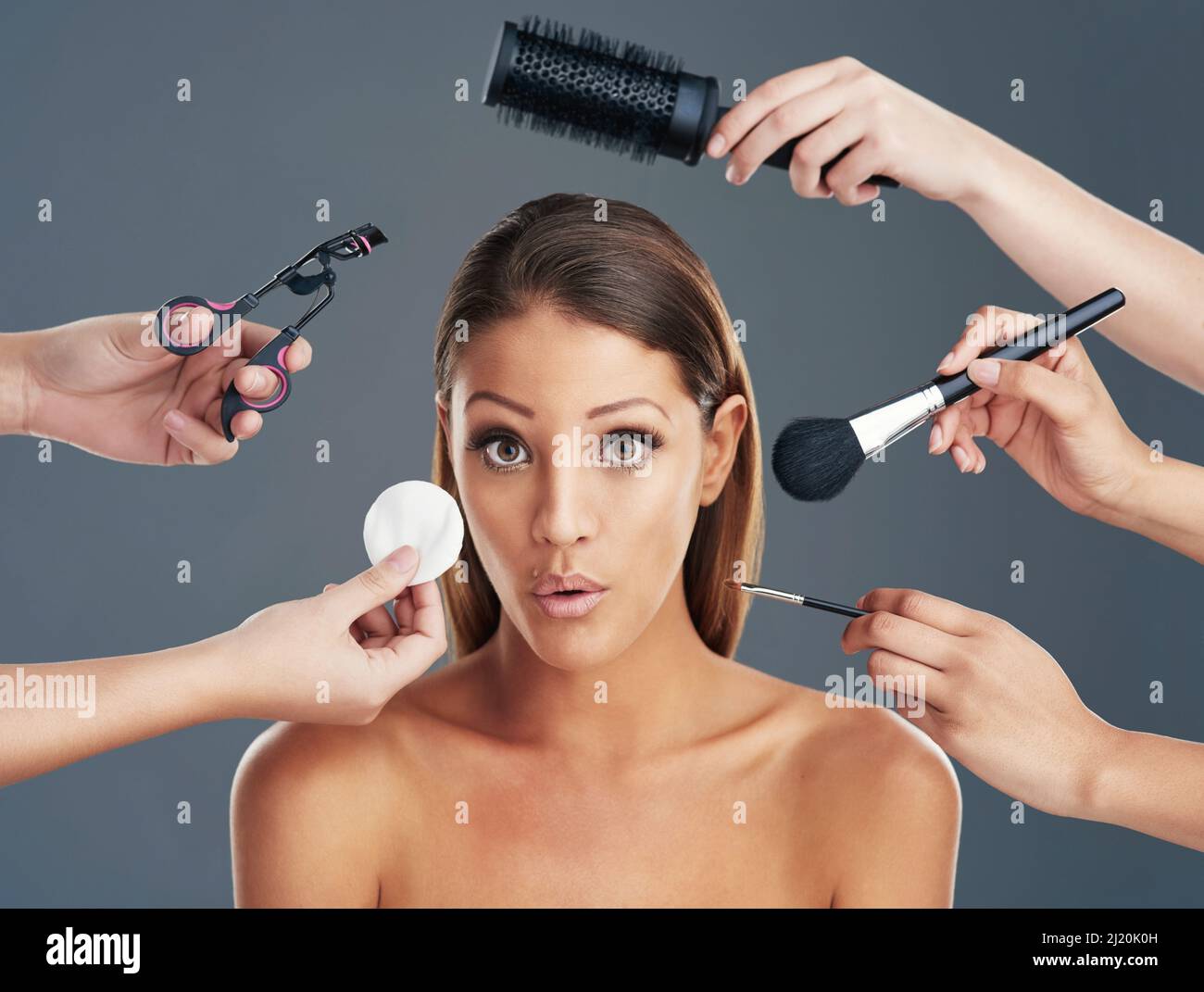 La folie du relooking. Photo portrait d'une belle jeune femme qui se fait  le maquillage et les cheveux sur un fond gris Photo Stock - Alamy