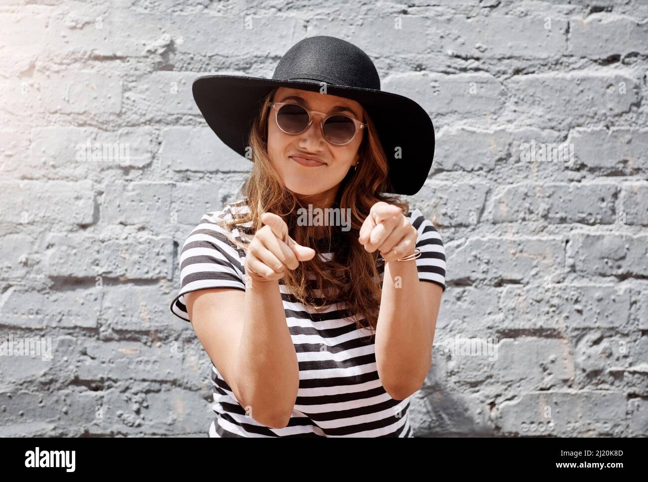 Vous avez vraiment bien compris. Portrait de jeune femme gaie pointant vers l'appareil photo avec les deux mains contre un mur de briques à l'extérieur. Banque D'Images