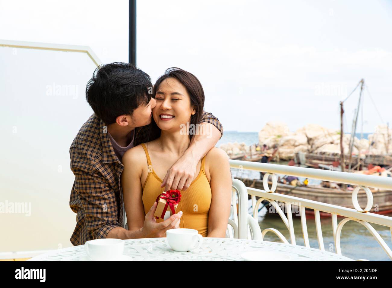 Un jeune couple souriant et embrassant donne des cadeaux au restaurant Ocean View - photo de stock Banque D'Images