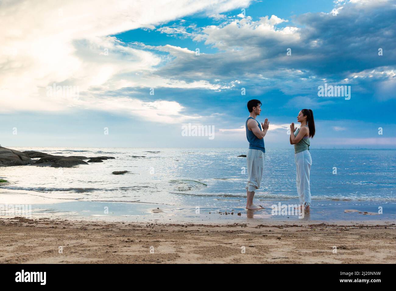Jeune couple pratiquant la méditation de yoga en se tenant sur la plage - photo de stock Banque D'Images
