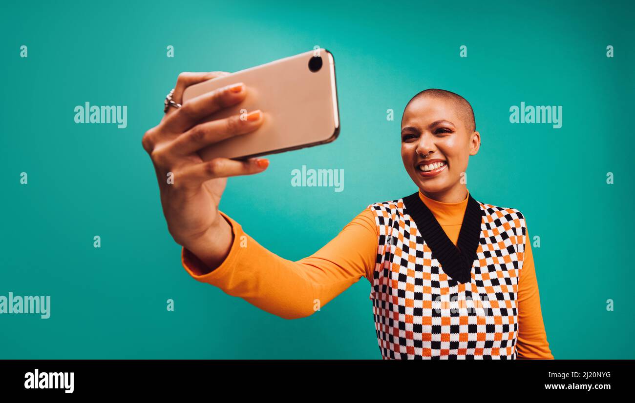 Sourire pour l'appareil photo. Jeune femme heureuse posant pour un autoportrait sur son appareil photo de smartphone. Jeune femme aux cheveux courts debout seul contre un tu Banque D'Images