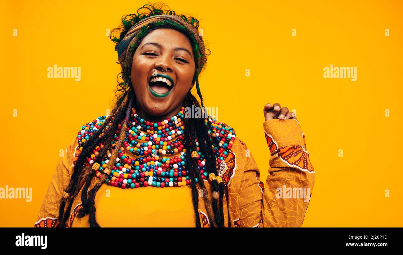 Femme ethnique excitée portant des vêtements culturels. Jeune femme à la mode souriant à l'appareil photo tout en se tenant debout sur un fond jaune. Youn élégant Banque D'Images