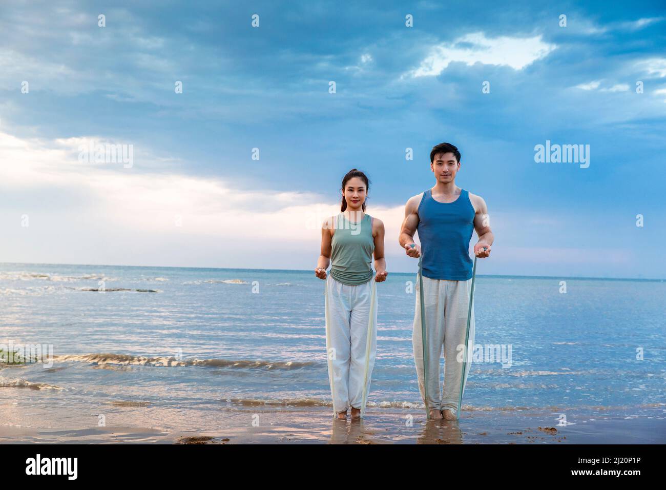 Jeune couple utilisant des bandes de résistance pour le yoga stretch à la plage - photo de stock Banque D'Images