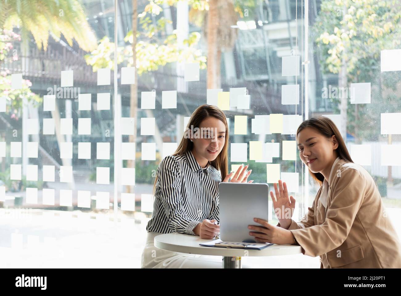 Deux femmes d'affaires asiatiques utilisant une tablette numérique parlent à leurs collègues de planifier leurs appels vidéo tout en travaillant intelligemment à la maison dans leur salon. Auto-isolation Banque D'Images