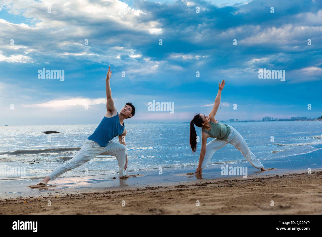 Jeune couple pratiquant le yoga s'étire sur la plage - photo de stock Banque D'Images