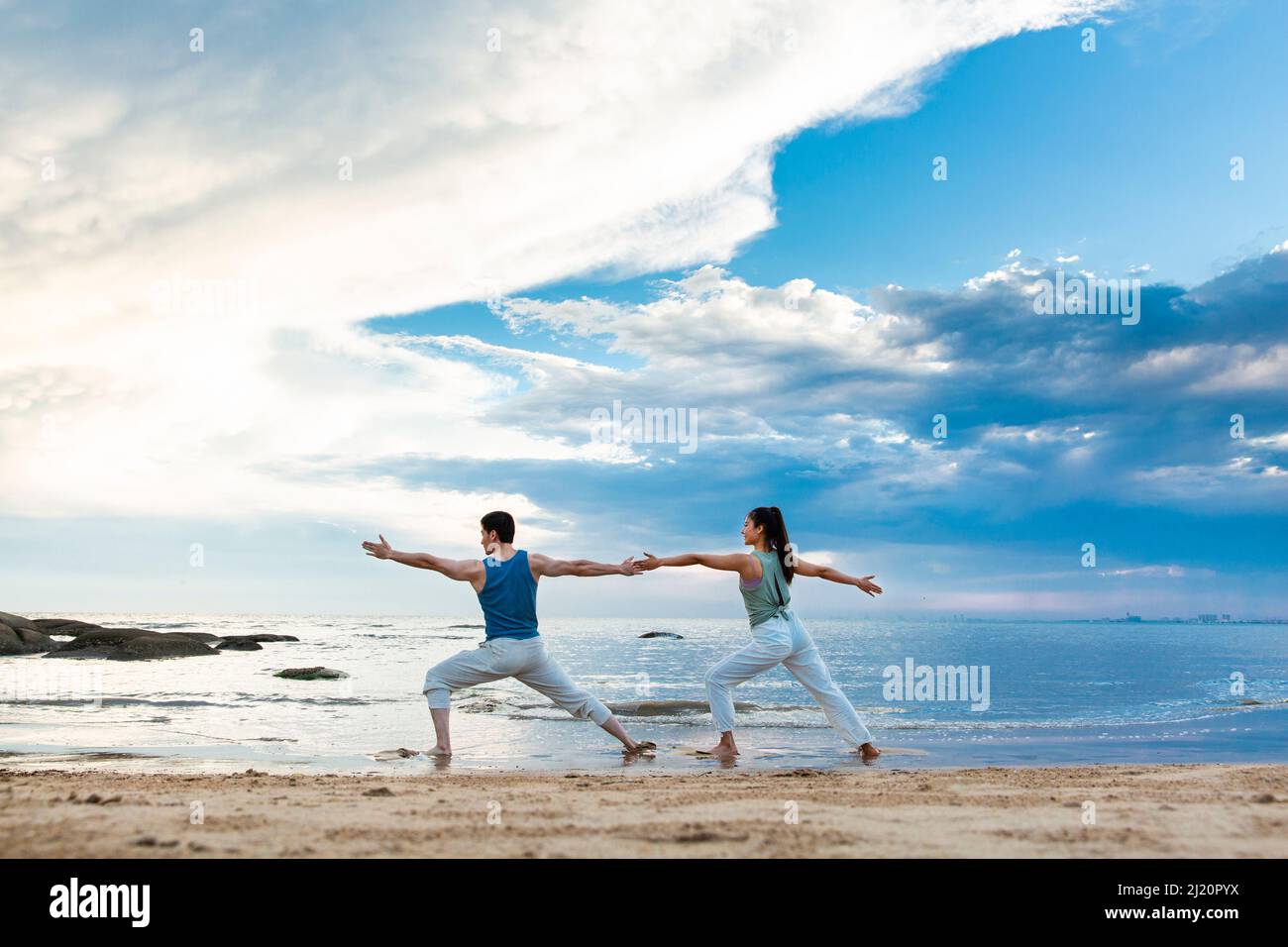 Jeune couple pratiquant le yoga s'étire sur la plage - photo de stock Banque D'Images
