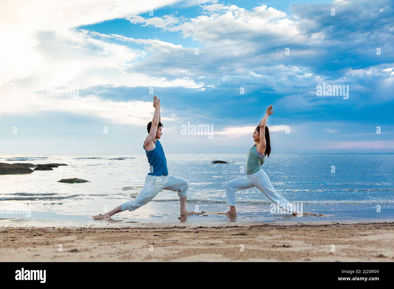 Jeune couple pratiquant le yoga s'étire sur la plage - photo de stock Banque D'Images