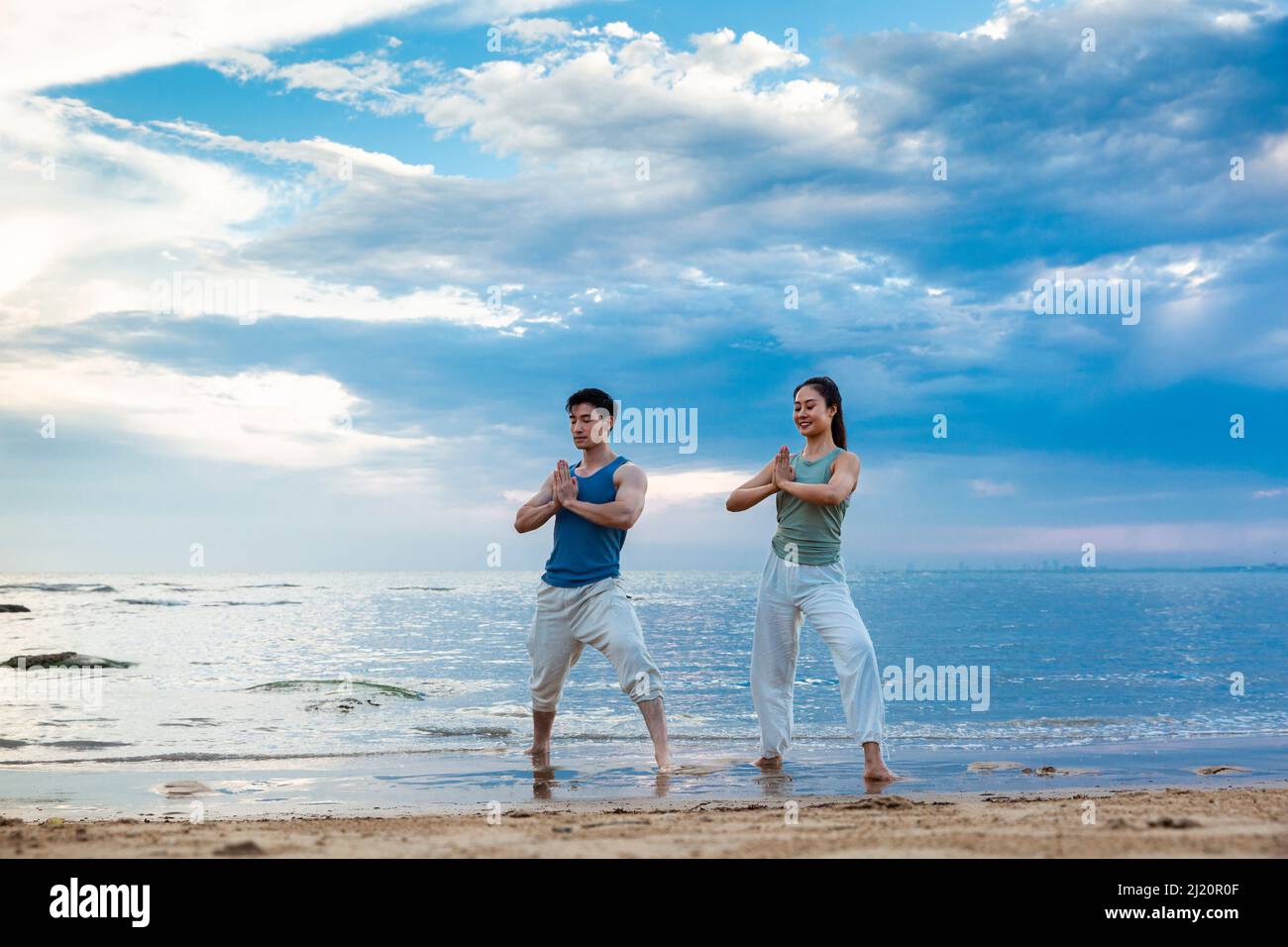 Jeune couple pratiquant la méditation de yoga en se tenant sur la plage - photo de stock Banque D'Images