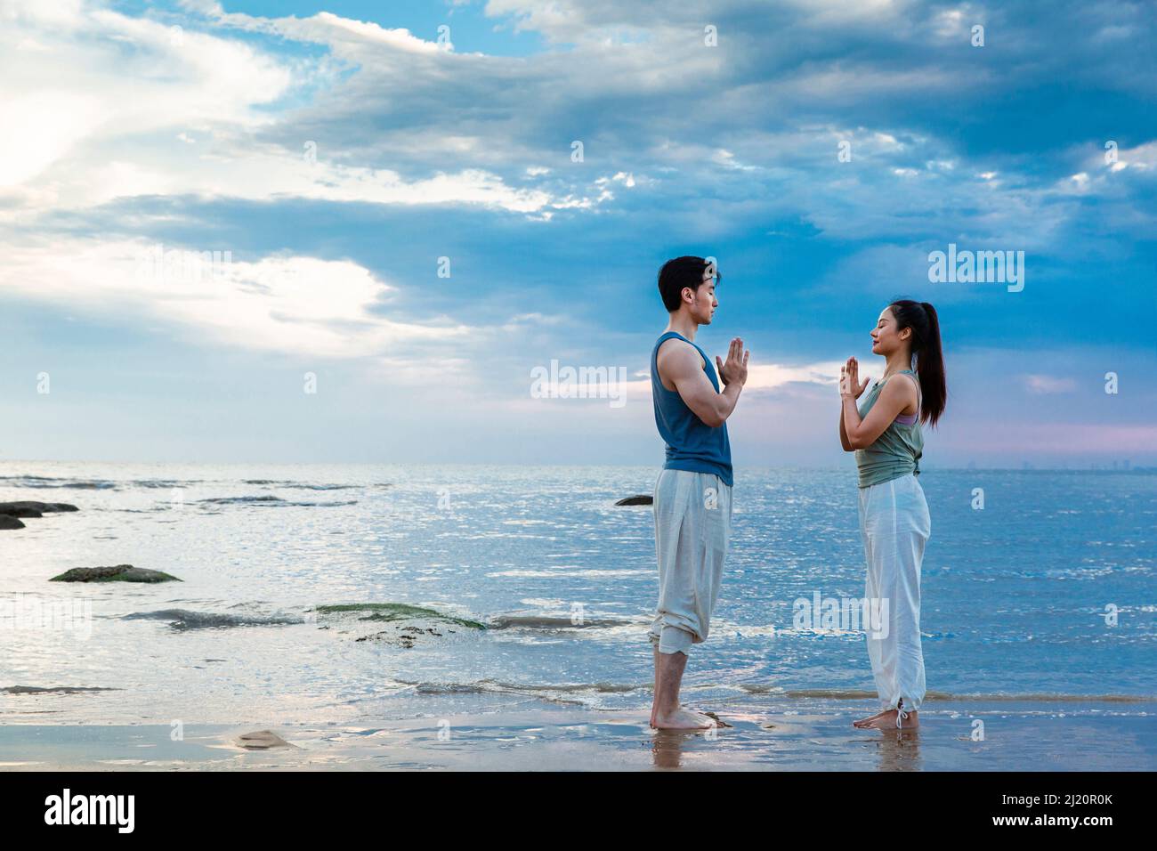 Jeune couple pratiquant la méditation de yoga en se tenant sur la plage - photo de stock Banque D'Images