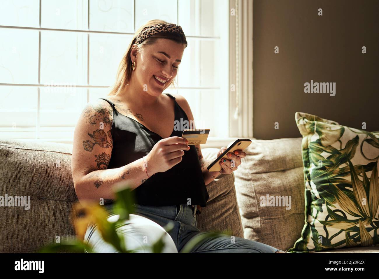 Jour de magasinage moins les files d'attente. Photo d'une jeune femme utilisant un smartphone et une carte de crédit sur le canapé à la maison. Banque D'Images