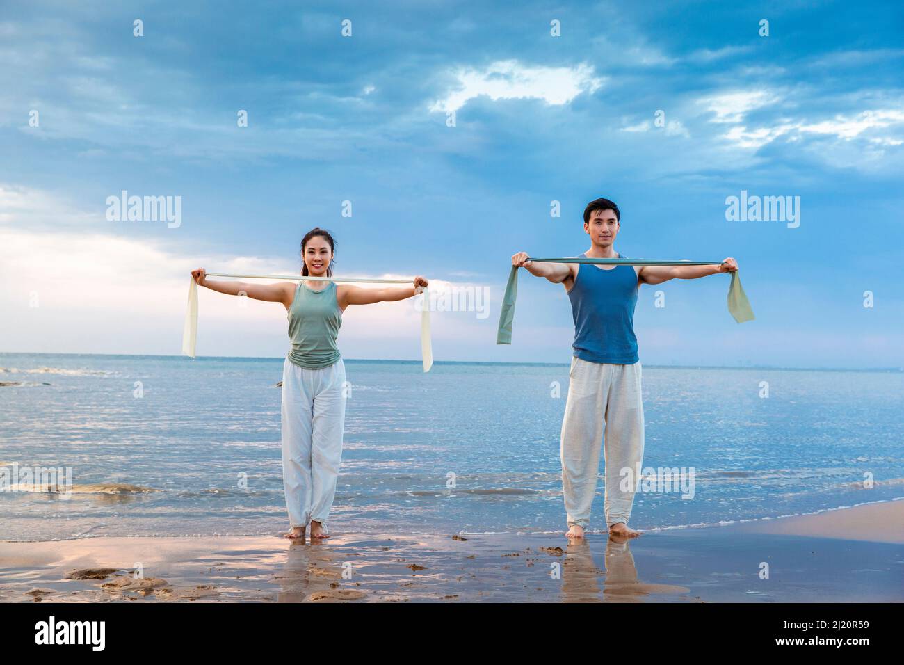 Jeune couple utilisant des bandes de résistance pour le yoga stretch à la plage - photo de stock Banque D'Images