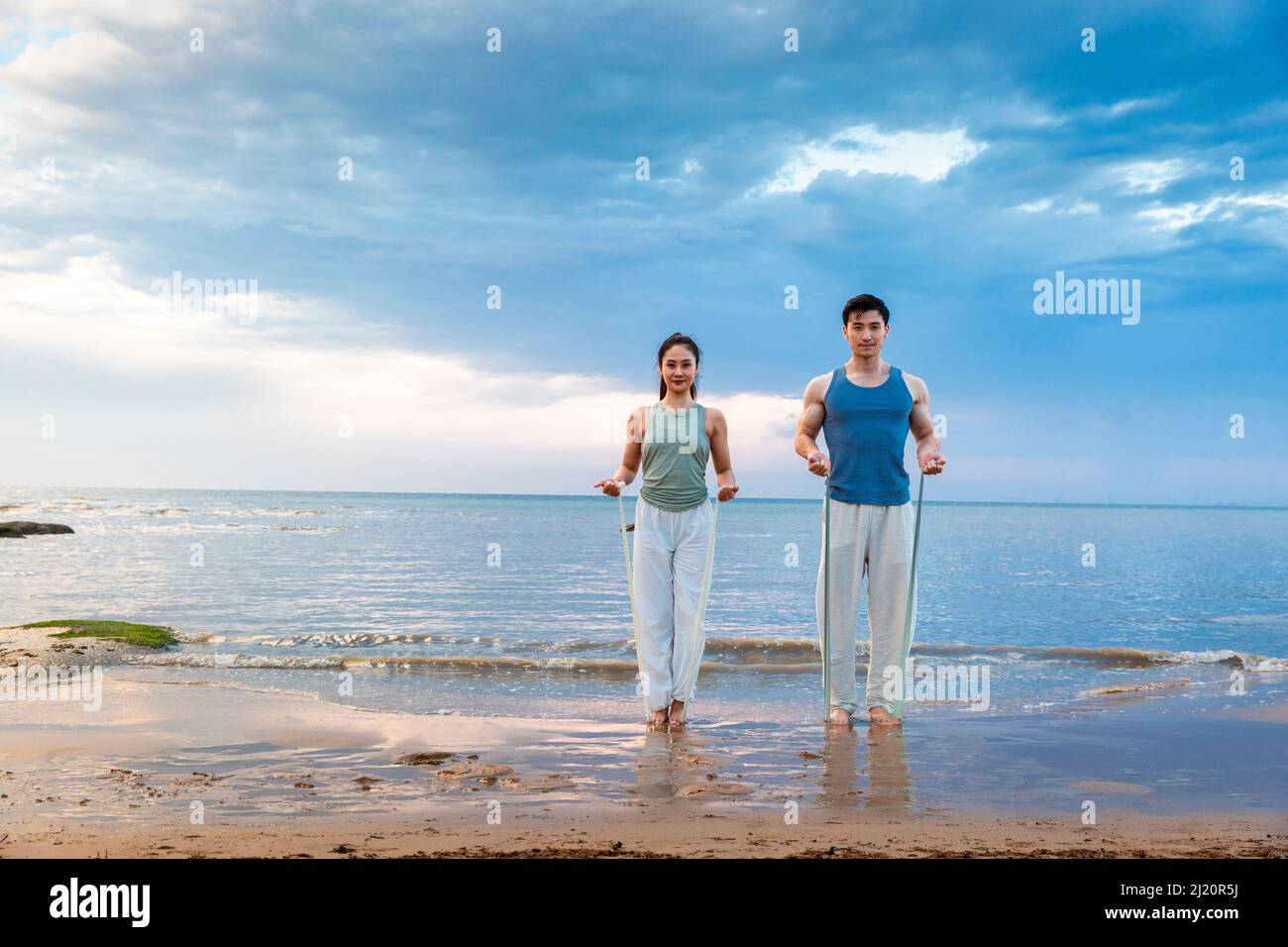 Jeune couple utilisant des bandes de résistance pour le yoga stretch à la plage - photo de stock Banque D'Images