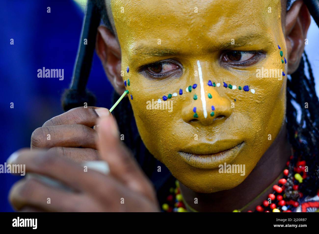 Homme de la tribu nomade de Wodaabe peint le visage pour la célébration de Gerepol, un rassemblement de clans différents dans lequel les femmes choisissent un mari. Robe pour hommes dans bes Banque D'Images
