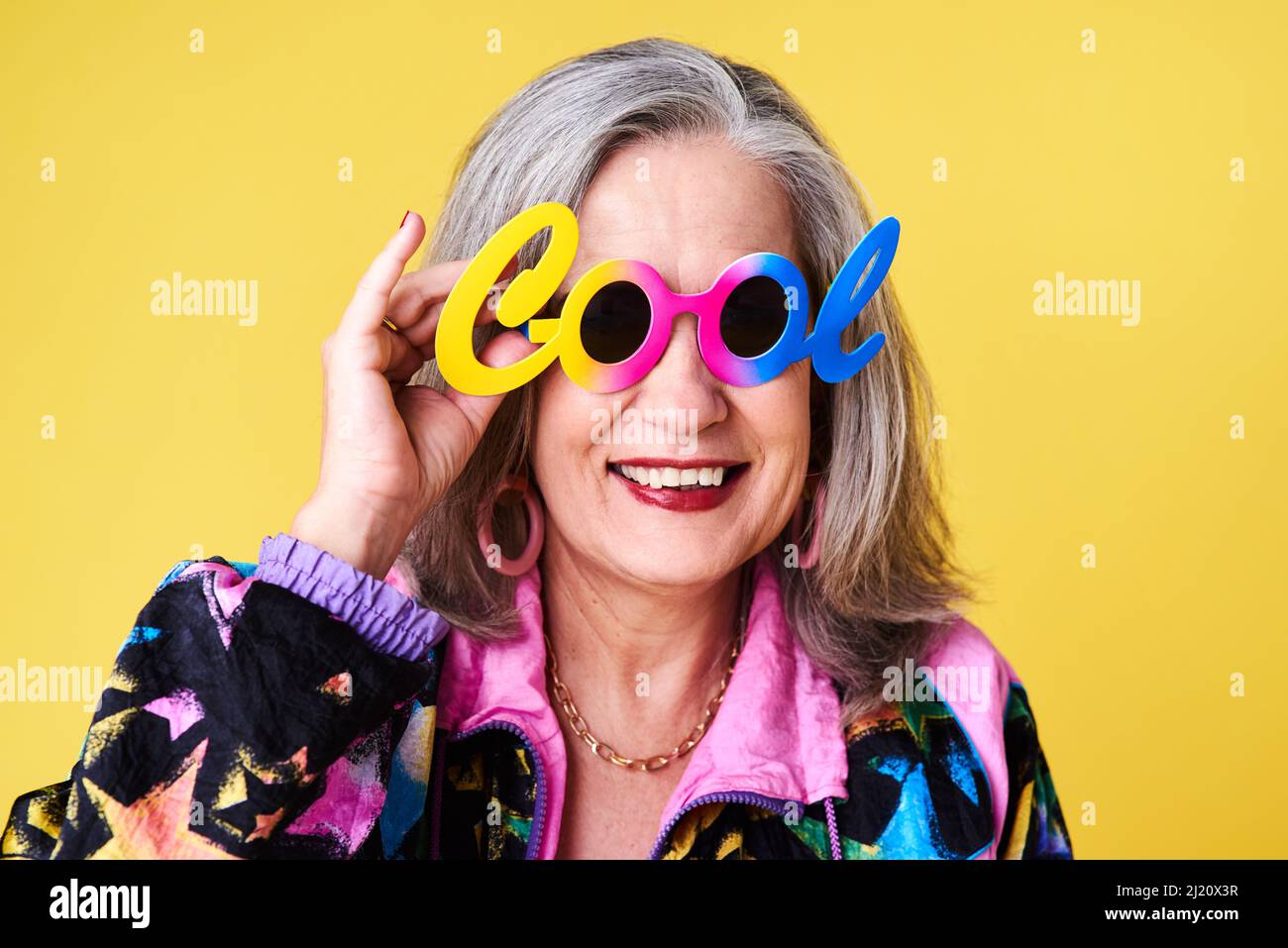 Je joue toujours au frais. Portrait d'une femme âgée confiante et élégante portant des lunettes de soleil se posant sur un fond jaune. Banque D'Images