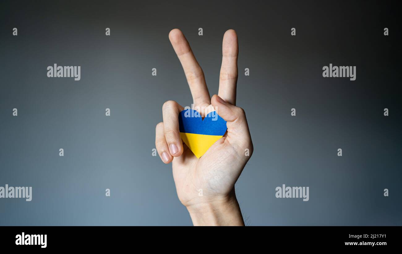 Drapeau de l'Ukraine couleur coeur dans la main faisant signe V. Banque D'Images