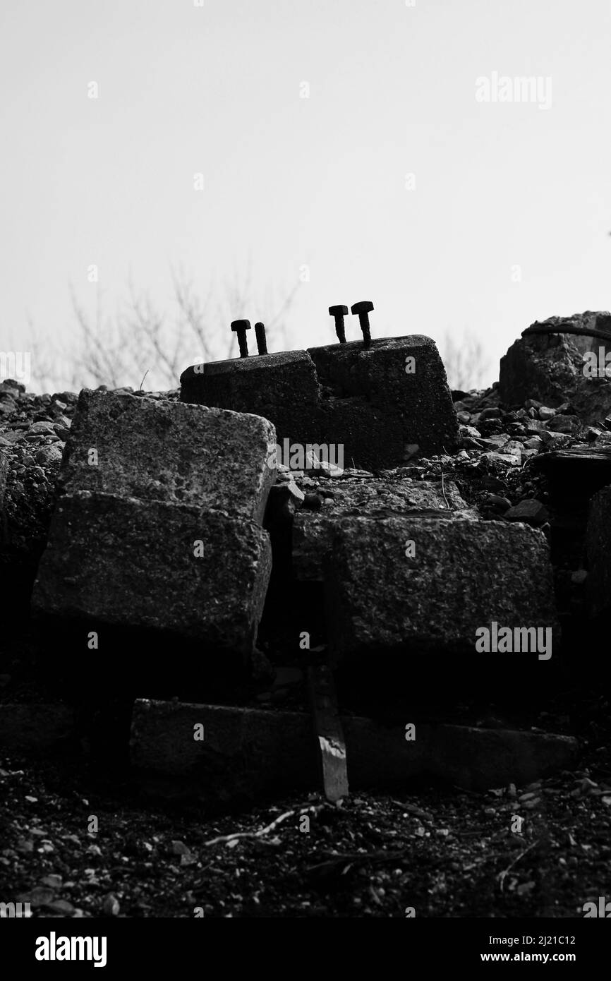 Les anciens boulons en acier qui collent du béton sont jetés sur le côté de la voie ferrée en noir et blanc. Banque D'Images