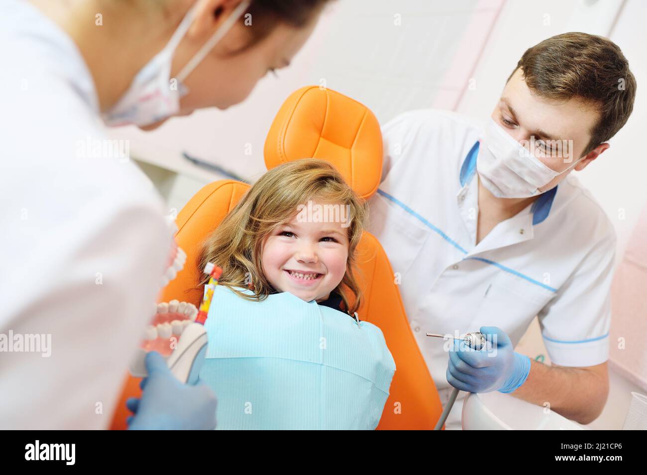 de jeunes dentistes, un homme et une femme, examinent les dents d'un patient d'enfant - une petite jolie fille assise dans une chaise dentaire orange. Banque D'Images