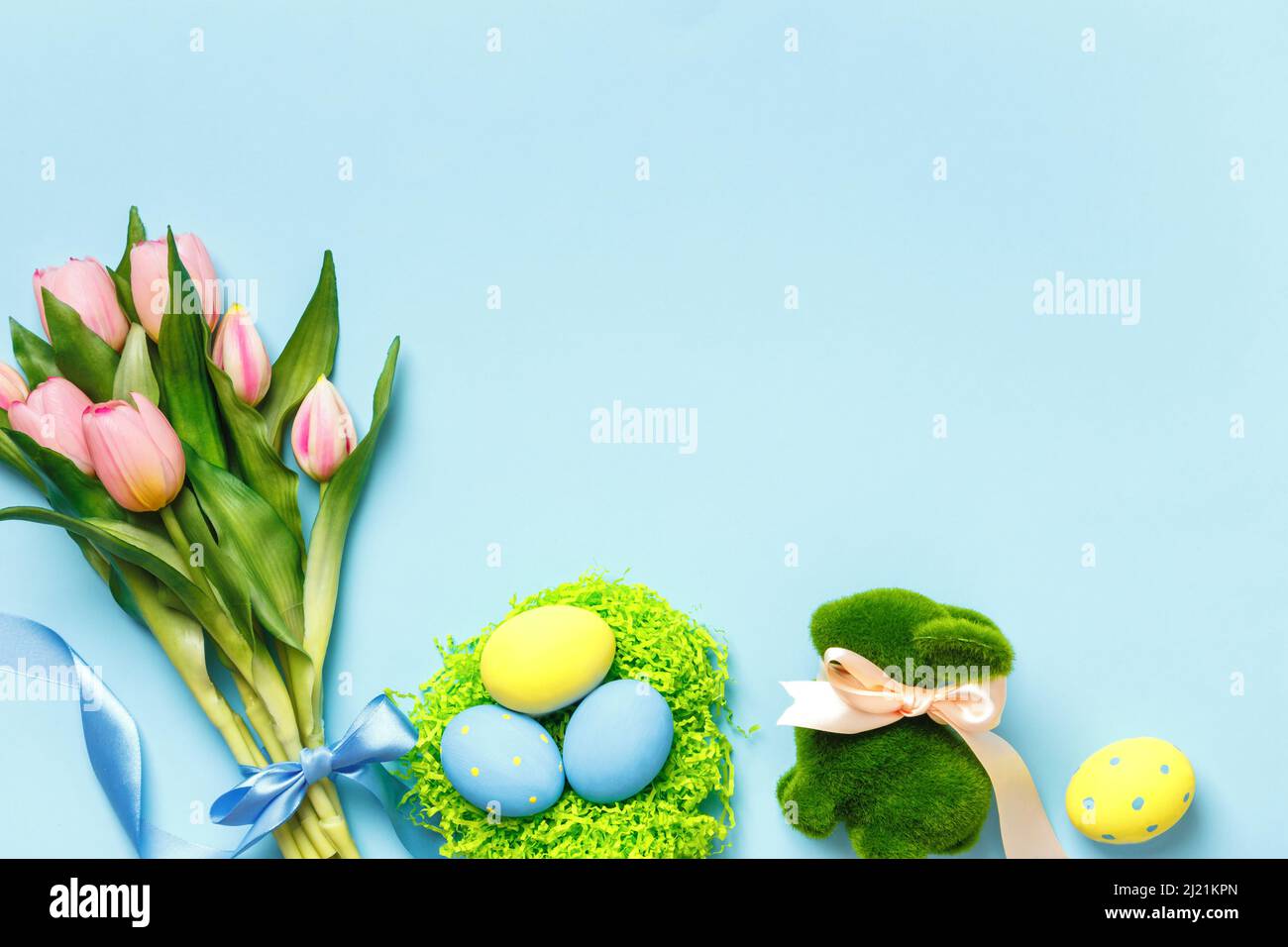 Composition de Pâques tulipes fleurs de printemps oeufs dans un nid jouet lapin sur fond bleu. Banque D'Images